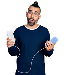 Hispanic man with ponytail holding portable battery charger afraid and shocked with surprise and amazed expression, fear and excited face.