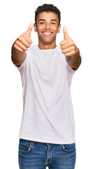 Fototapeta premium Young handsome african american man wearing casual white tshirt approving doing positive gesture with hand, thumbs up smiling and happy for success. winner gesture.
