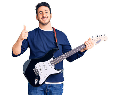 Young hispanic man playing electric guitar smiling happy and positive, thumb up doing excellent and approval sign