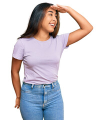 Young latin woman wearing casual clothes very happy and smiling looking far away with hand over head. searching concept.