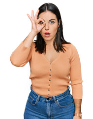 Fototapeta premium Young hispanic woman wearing casual clothes doing ok gesture shocked with surprised face, eye looking through fingers. unbelieving expression.