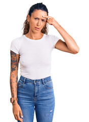 Young hispanic woman with tattoo wearing casual white tshirt pointing unhappy to pimple on...