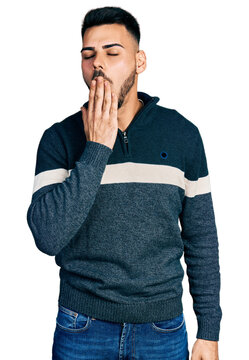 Young hispanic man with beard wearing casual winter sweater bored yawning tired covering mouth with hand. restless and sleepiness.