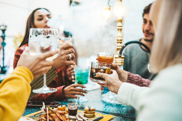 Happy friends drinking cocktails and smoking shisha in hookah lounge bar - Multiethnic young people hanging out having weekend party together - Concept about friendship, beverage and youth culture