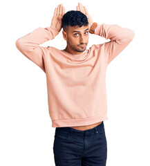 Young hispanic man wearing casual clothes doing bunny ears gesture with hands palms looking cynical and skeptical. easter rabbit concept.
