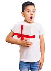 Little cute boy kid holding gift scared and amazed with open mouth for surprise, disbelief face