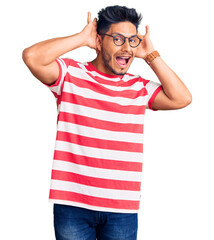 Handsome latin american young man wearing casual clothes and glasses smiling cheerful playing peek a boo with hands showing face. surprised and exited