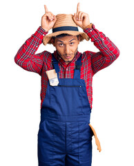Handsome latin american young man weaing handyman uniform doing funny gesture with finger over head...