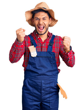 Handsome latin american young man weaing handyman uniform angry and mad raising fists frustrated and furious while shouting with anger. rage and aggressive concept.