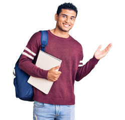 Hispanic handsome young man wearing student backpack and notebook celebrating victory with happy smile and winner expression with raised hands - obrazy, fototapety, plakaty