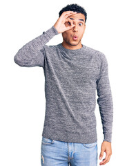 Hispanic handsome young man wearing casual sweater doing ok gesture shocked with surprised face, eye looking through fingers. unbelieving expression.