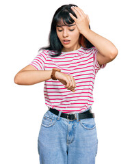 Young hispanic girl wearing casual clothes looking at the watch time worried, afraid of getting late