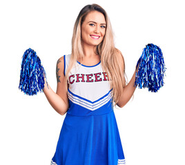 Young beautiful blonde woman wearing cheerleader uniform holding pompom looking positive and happy...