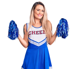 Young beautiful blonde woman wearing cheerleader uniform holding pompom looking positive and happy standing and smiling with a confident smile showing teeth