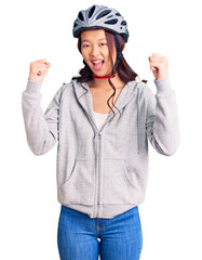 Young beautiful chinese girl wearing bike helmet screaming proud, celebrating victory and success very excited with raised arms