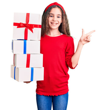 Cute hispanic child girl holding gift smiling happy pointing with hand and finger to the side