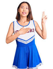 Young beautiful chinese girl wearing cheerleader uniform smiling swearing with hand on chest and...