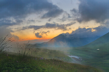 Fototapeta premium Sunset, sunrise in the mountains at a height evening morning in fog with a mountain lake with flowers in the foreground