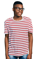 Young african american man wearing casual t shirt and glasses smiling looking to the side and...