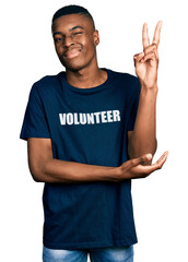 Young african american man wearing volunteer t shirt smiling with happy face winking at the camera doing victory sign with fingers. number two.