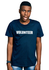 Young african american man wearing volunteer t shirt in shock face, looking skeptical and sarcastic, surprised with open mouth