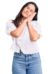 Young beautiful brunette woman wearing casual shirt sleeping tired dreaming and posing with hands together while smiling with closed eyes.