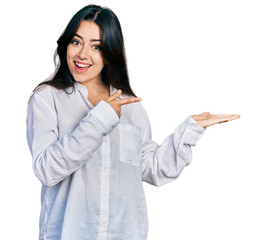 Beautiful hispanic woman wearing casual white shirt amazed and smiling to the camera while presenting with hand and pointing with finger.