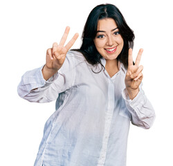 Beautiful hispanic woman wearing casual white shirt smiling looking to the camera showing fingers doing victory sign. number two.