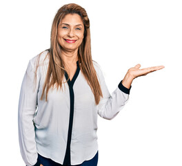 Middle age latin woman wearing business shirt smiling cheerful presenting and pointing with palm of hand looking at the camera.