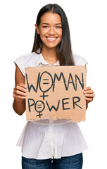 Beautiful hispanic woman holding woman power banner looking positive and happy standing and smiling with a confident smile showing teeth