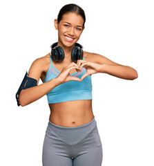Beautiful hispanic woman wearing sportswear and headphones smiling in love showing heart symbol and shape with hands. romantic concept.