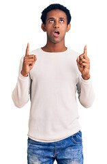 African handsome man wearing casual winter sweater amazed and surprised looking up and pointing...