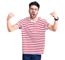 Naklejka premium Young hispanic man wearing casual clothes angry and mad raising fists frustrated and furious while shouting with anger. rage and aggressive concept.
