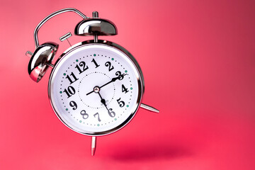 silver vintage alarm clock falls on the floor with a dark pink background
