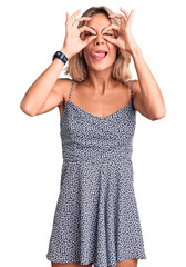 Beautiful caucasian woman wearing summer dress doing ok gesture like binoculars sticking tongue out, eyes looking through fingers. crazy expression.