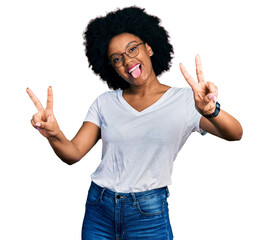 Young african american woman wearing casual white t shirt smiling with tongue out showing fingers of both hands doing victory sign. number two.