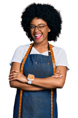 Young african american woman dressmaker designer wearing atelier apron winking looking at the...