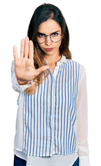 Beautiful hispanic woman wearing casual striped shirt doing stop sing with palm of the hand. warning expression with negative and serious gesture on the face.