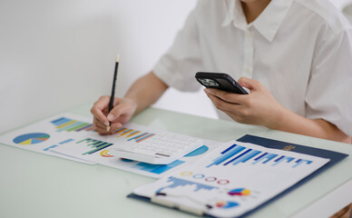 Fototapeta premium Asian woman at desk using smartphone financial app and doing reports close hand in hand.