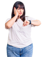 Young plus size woman wearing casual clothes looking at the watch time worried, afraid of getting late