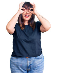 Obraz na płótnie Canvas Young plus size woman wearing casual clothes doing ok gesture like binoculars sticking tongue out, eyes looking through fingers. crazy expression.