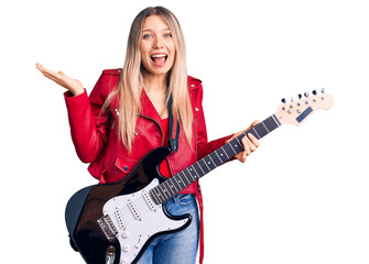 Fototapeta premium Young beautiful blonde woman playing electric guitar celebrating victory with happy smile and winner expression with raised hands