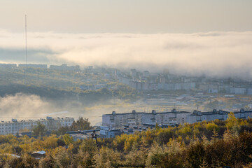 Beautiful morning foggy cityscape. View of the residential city blocks in the clouds. Buildings in the fog. Low clouds. City of Magadan, Magadan region, Siberia, Far East of Russia. Autumn season.