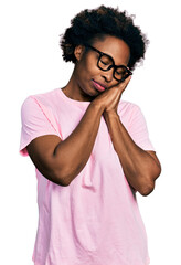 African american woman with afro hair wearing casual clothes and glasses sleeping tired dreaming and posing with hands together while smiling with closed eyes.