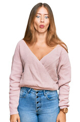 Beautiful blonde woman wearing casual winter pink sweater making fish face with lips, crazy and comical gesture. funny expression.