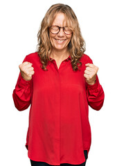 Middle age blonde woman wearing casual shirt over red background excited for success with arms raised and eyes closed celebrating victory smiling. winner concept.