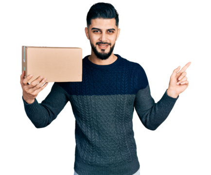 Young arab man with beard holding delivery package smiling happy pointing with hand and finger to the side