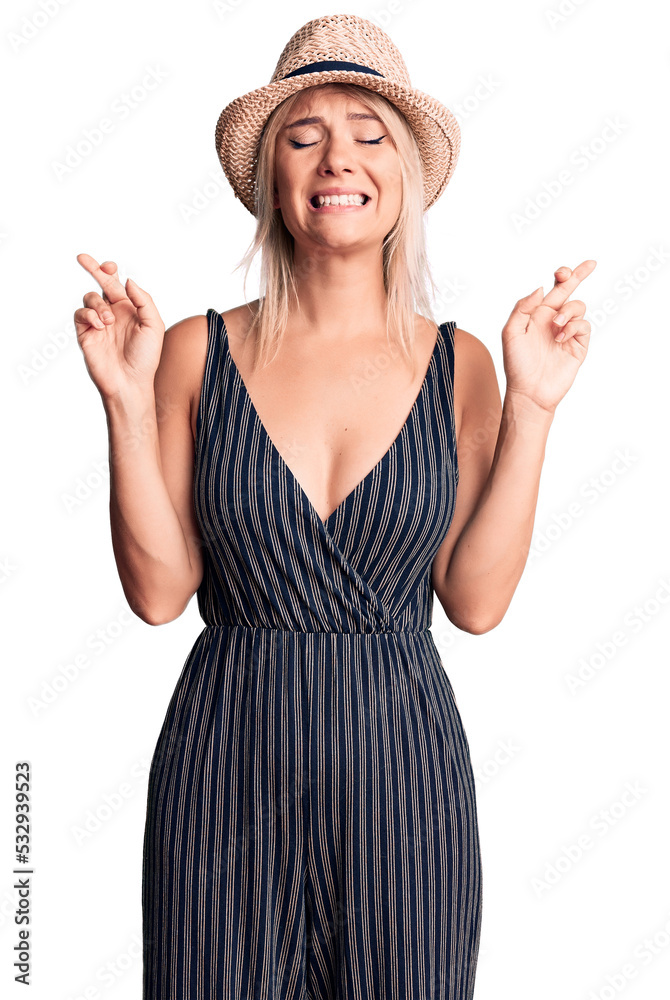 Sticker Young beautiful blonde woman wearing summer hat and dress gesturing finger crossed smiling with hope and eyes closed. luck and superstitious concept.