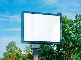blank advertising sign in front of green trees and blue sky