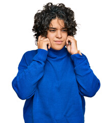 Young hispanic woman with curly hair wearing turtleneck sweater covering ears with fingers with annoyed expression for the noise of loud music. deaf concept.